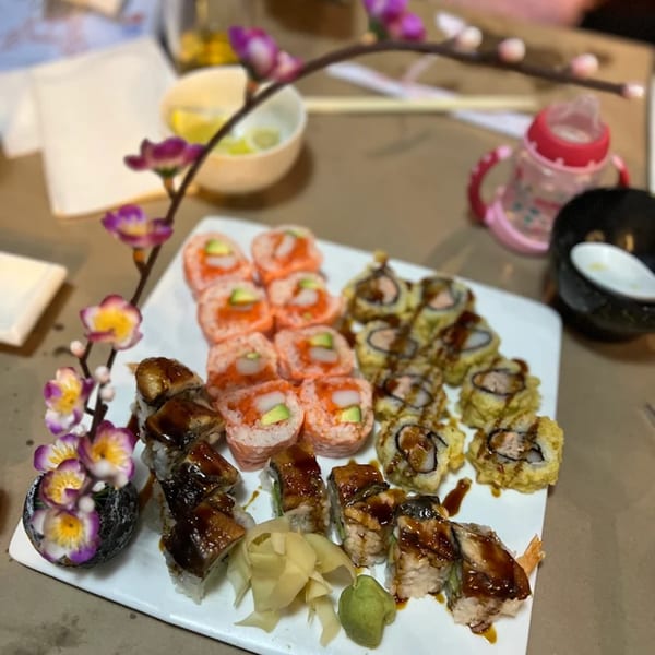 A white plate of various sushi rolls, including eel, shrimp, and fried tempura, with ginger and wasabi.
