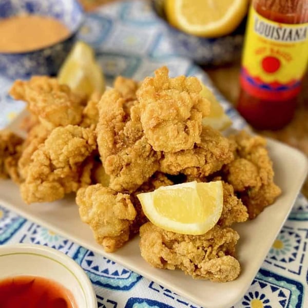 Crispy fried Japanese seafood with lemon wedges, hot sauce, and dipping sauces on a patterned cloth.